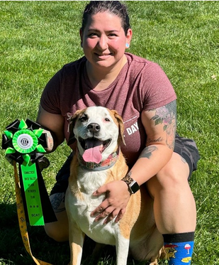 Sarafina, veterinary technician, seated outdoors with a dog and award ribbon